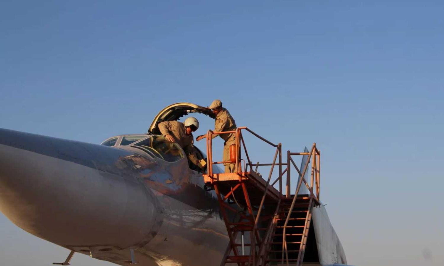 طيارون روس يتعاملون مع طائرة حربية روسية في قاعدة حميميم الجوية بريف محافظة اللاذقية على الساحل السوري (سبوتنيك)